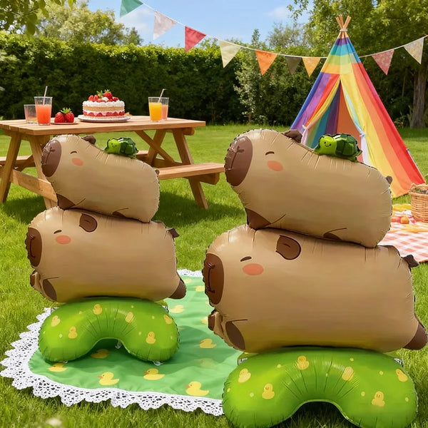 Several tan foil balloon shaped like capybaras are displayed outdoors on a green blanket.