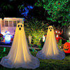 A white ghost decoration with a glowing face is displayed outdoors in a garden setting.