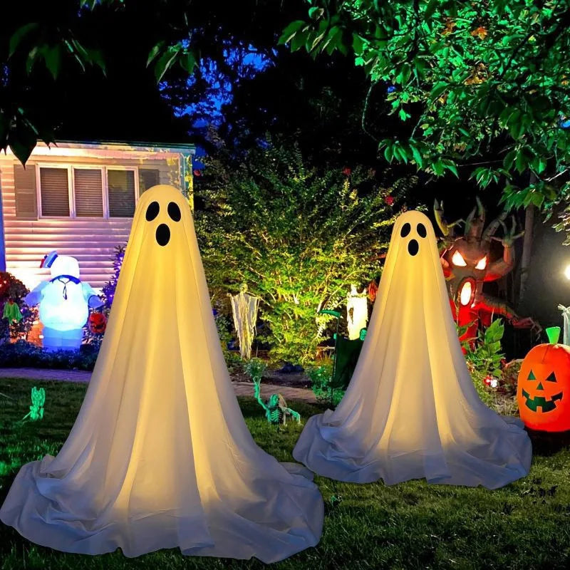 A white ghost decoration with a glowing face is displayed outdoors in a garden setting.