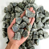 A hand holds a pile of natural raw healing crystal stones for chakra balancing and home decor