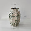A rustic ceramic milk pitcher with a cracked glaze and pastoral floral design, shown against a white background.