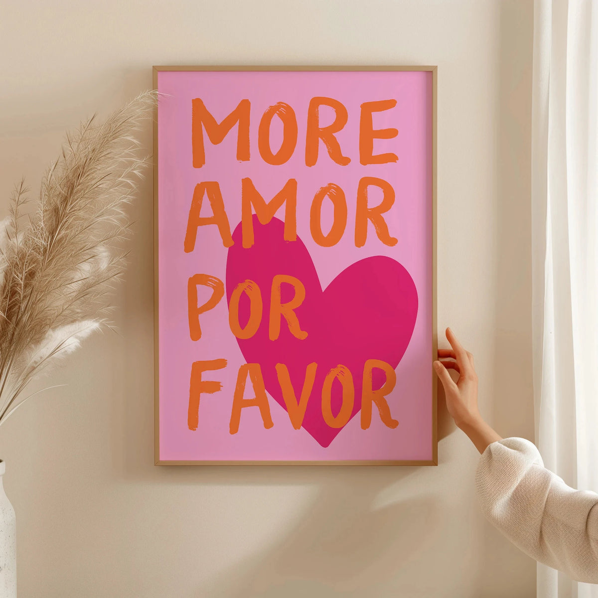 A pink canvas wall art print featuring the text MORE AMOR POR FAVOR in orange and magenta script on a light beige wall.