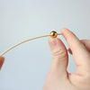 A hand holds a thin bamboo skewer with a gold accent ball tip against a light background.