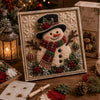 A framed 3D fabric poke art kit featuring a detailed snowman and winter forest scene with evergreen branches and berries.