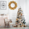 A golden silk Christmas ball wreath ornament displayed on a white wall next to a decorated Christmas tree and antique chair.