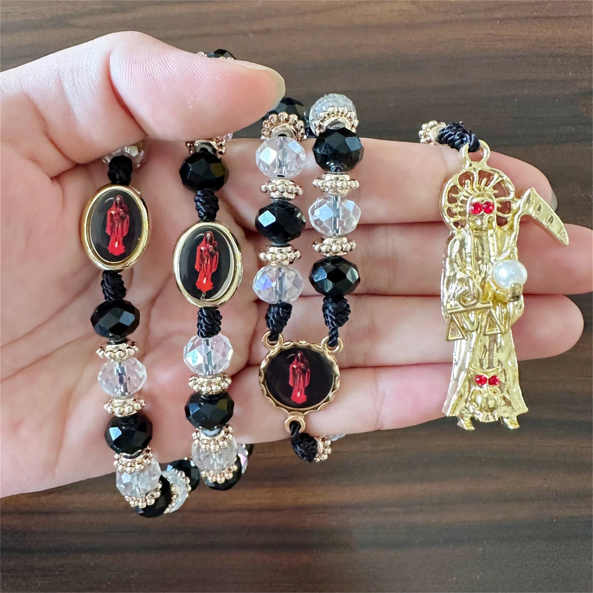 A gold and black rosary necklace featuring a figure of Santa Muerte with a red ribbon.