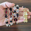 A gold and black rosary necklace featuring a figure of Santa Muerte with a red ribbon.