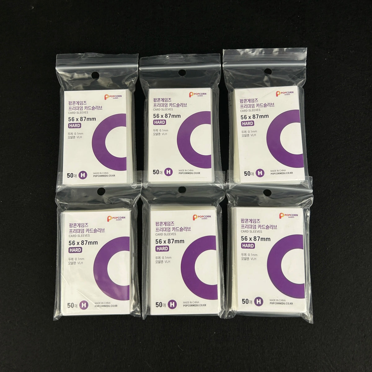 Five packs of clear protective card sleeves with purple and white labels are displayed on a dark surface.