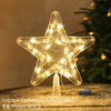 A clear LED Christmas tree star topper with warm white lights resting on a wooden surface.