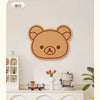 A round, brown felt wall decor panel shaped like a bear face is mounted on a white wall.