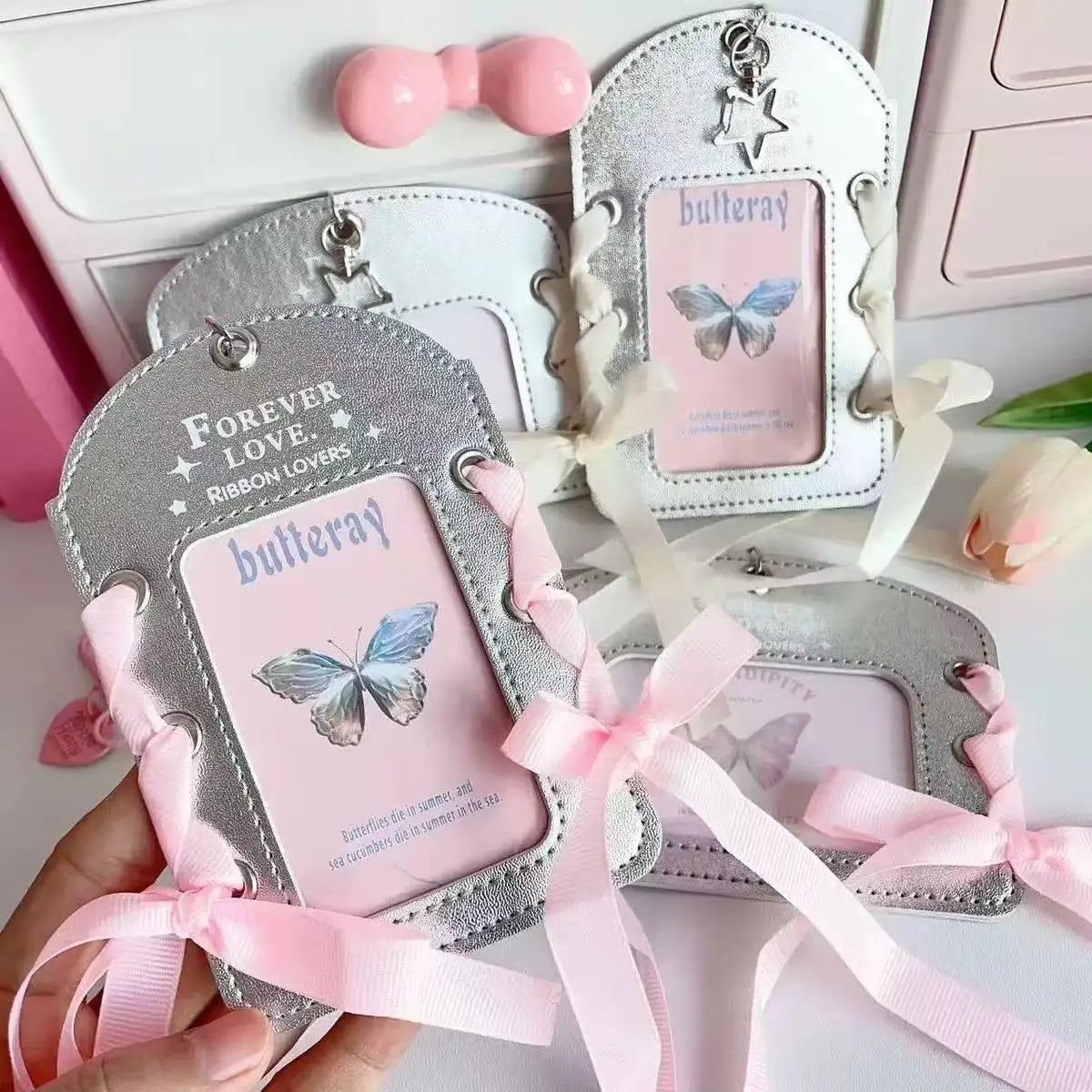 A hand holds a silver lace PU card holder with a pink ribbon bow keychain and matching butterfly charm.