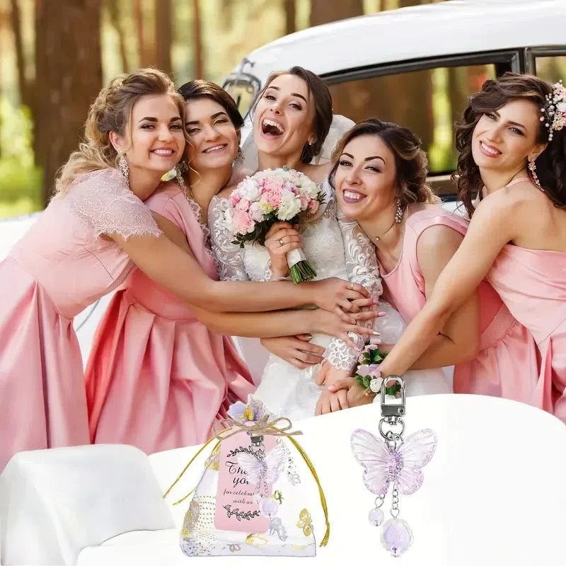 A group of women in pink dresses posing with a white car, holding a pink butterfly pendant keychain set.