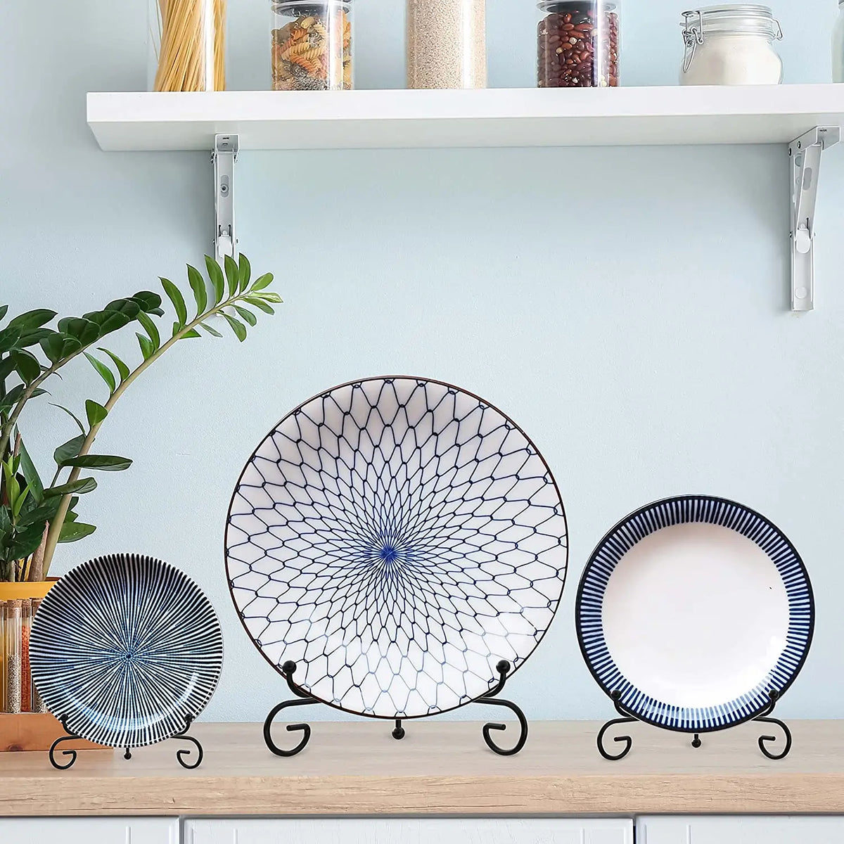 Three decorative metal display easels holding plates and collectibles on a light blue shelf.