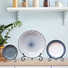 Three decorative metal display easels holding plates and collectibles on a light blue shelf.
