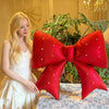 A large, bright red decorative pearl bow balloon weight is displayed on a table in front of a woman.