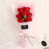 A pink glass vase holds a bouquet of red roses with a black tag and natural twine bow.