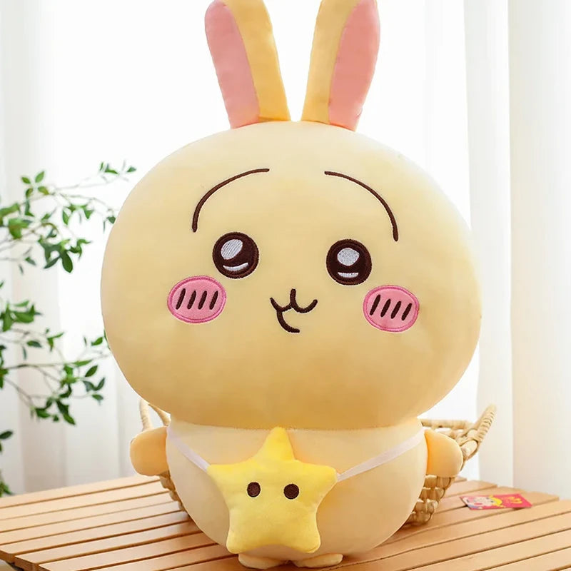 A yellow Chiikawa Hachiware plush pillow with pink accents sitting on a wooden surface.