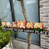 A rustic wooden hanging sign featuring several orange and white cat figurines attached to a tree branch.