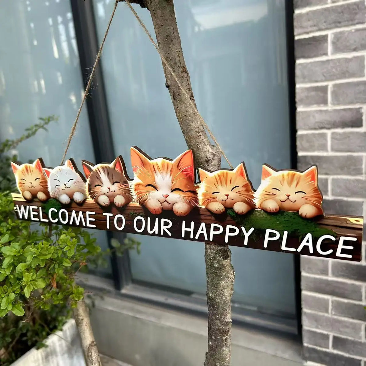 A rustic wooden hanging sign featuring several orange and white cat figurines attached to a tree branch.