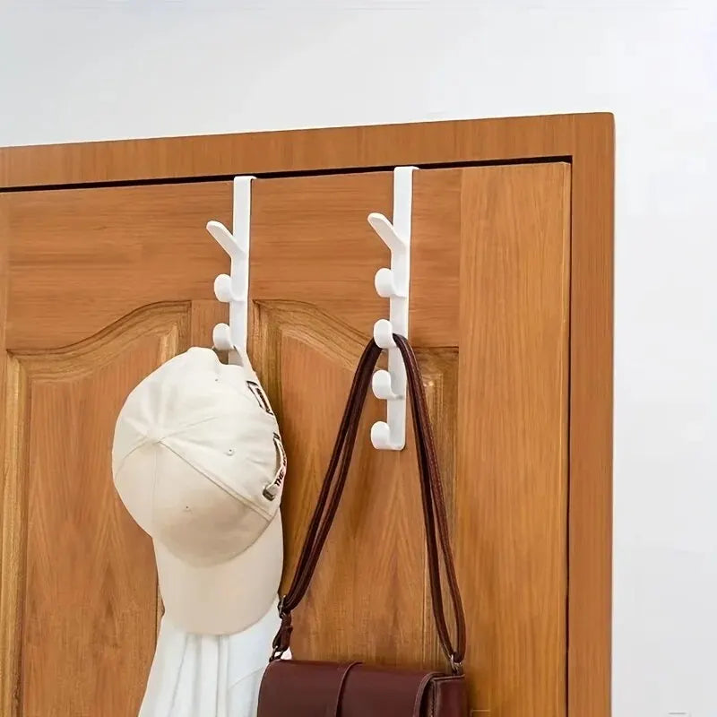 A beige baseball cap is hanging on over-the-door hooks on a wooden cabinet door.