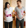 A pregnant woman is shown holding her belly while a man stands beside her, both smiling and touching hands.