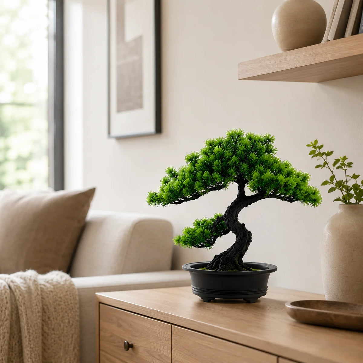 An artificial bonsai pine tree in a black pot sits on a wooden cabinet next to a sofa.
