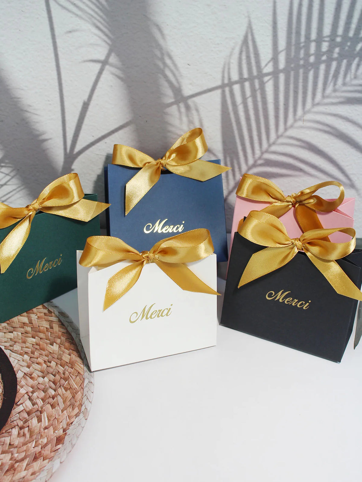 A collection of elegant paperboard thank you gift bags in various shades of blue, green, and black tied with gold ribbon.