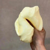 A hand is squeezing a large, pale yellow cheese cube stress ball fidget toy against a neutral background.