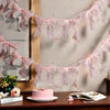 Pink tulle bow garland for party decor displayed against a neutral background with a cake and book.
