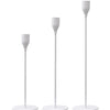 A set of three elegant metal candle holders with slender white candles displayed on a dark surface.