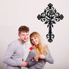 A young couple smiling while holding a black decorative metal cross wall art design.