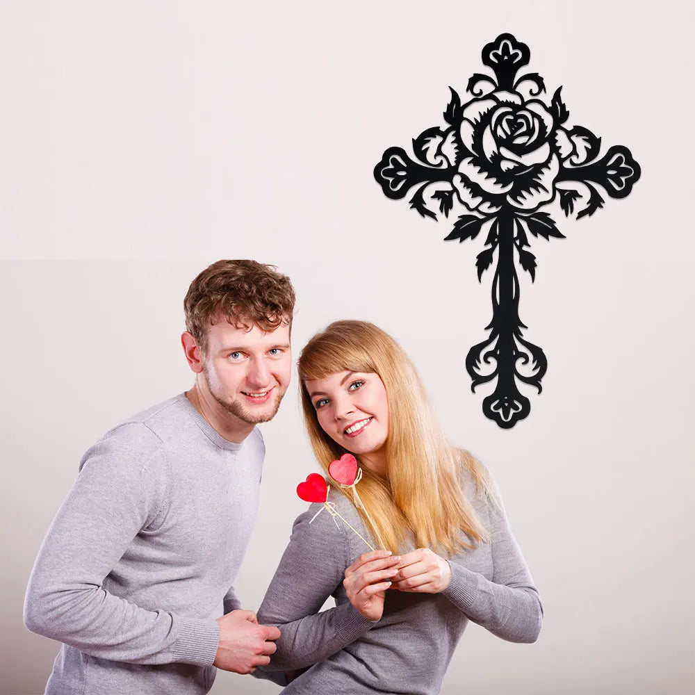 A young couple smiling while holding a black decorative metal cross wall art design.