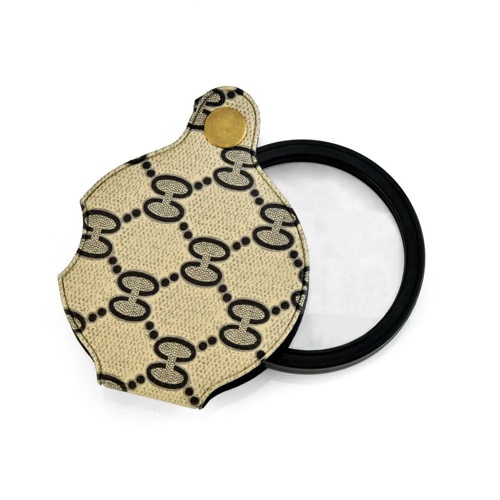 A pocket magnifier with a light beige patterned leather case and a gold-colored keychain.
