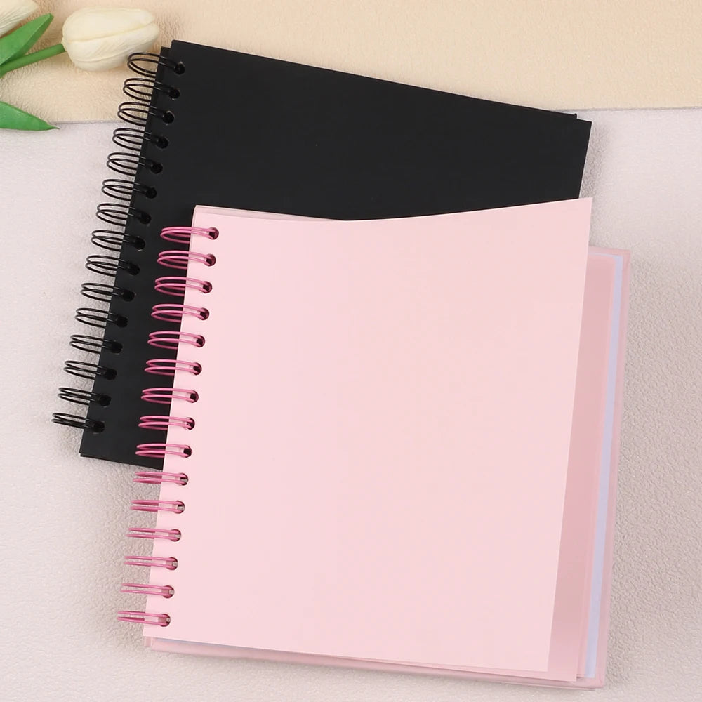 A pink spiral-bound notebook lies beneath a black notebook on a light surface.