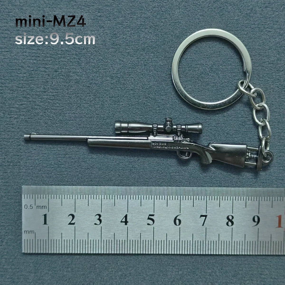 A miniature alloy gun model keychain with a silver finish is shown next to a ruler.