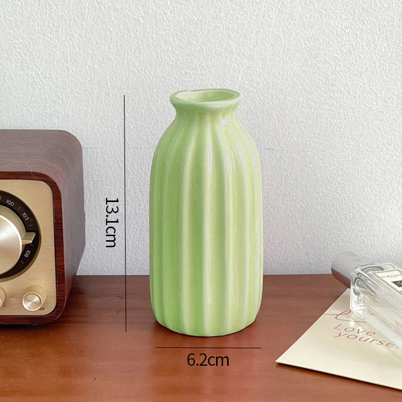 A tall, light green ceramic bud vase with vertical ridges sits on a wooden surface.