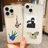 A hand holds a clear phone case featuring black and white graffiti stickers on a light beige background.
