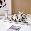 Silver resin letters spelling LOVE with a small bird silhouette on a white surface.