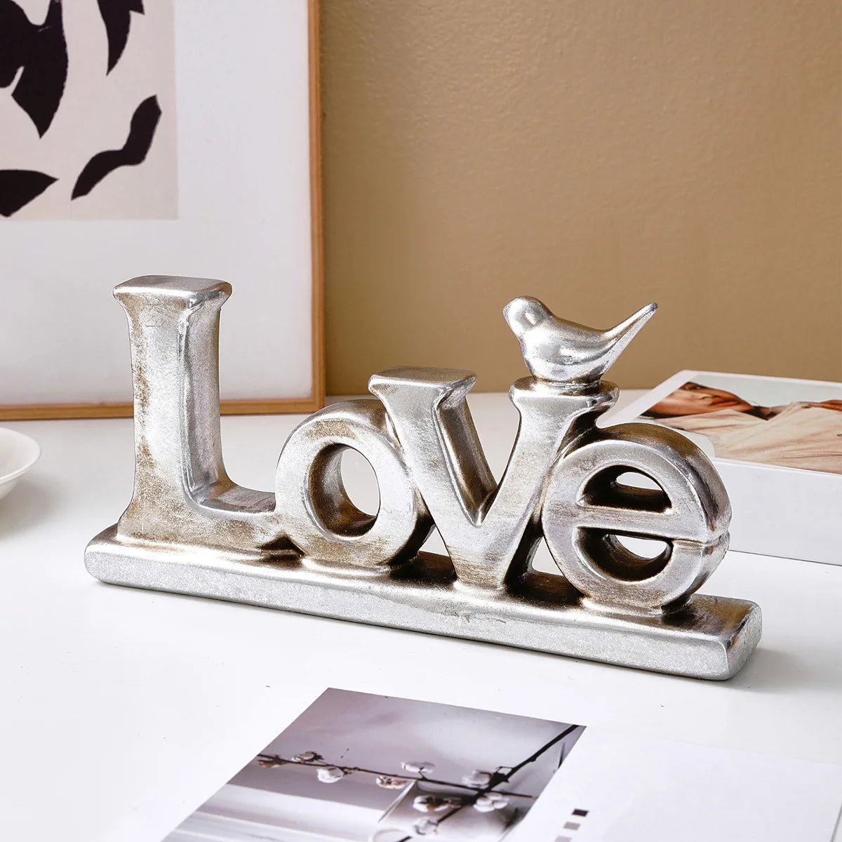 Silver resin letters spelling LOVE with a small bird silhouette on a white surface.