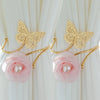 A set of two gold-toned decorative flower butterfly curtain tiebacks with pink roses and pearl accents.