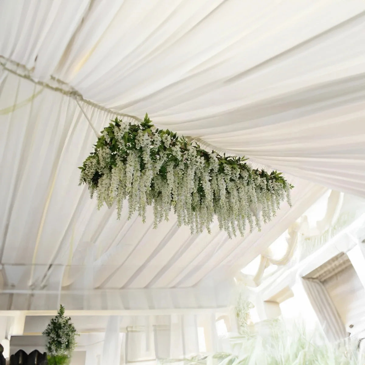A cascading garland of white silk wisteria vines hanging from a white draped ceiling.