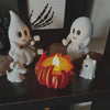 A set of white ghost figures and a red candle arranged on a dark surface for Halloween decor.