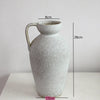 A tall, light gray ceramic vase with a handle, shown against a white background.