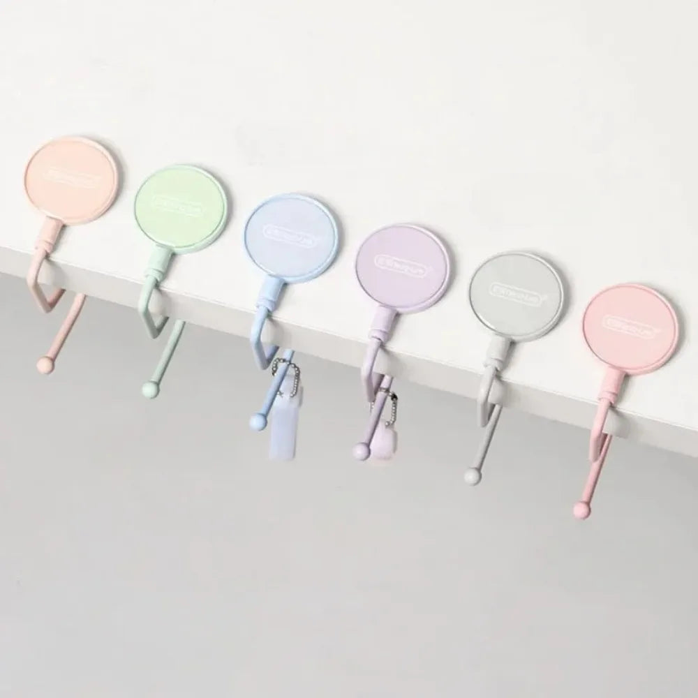 A row of colorful heavy duty purse and bag hooks in pastel shades pink, mint green, and lavender mounted on a white surface.