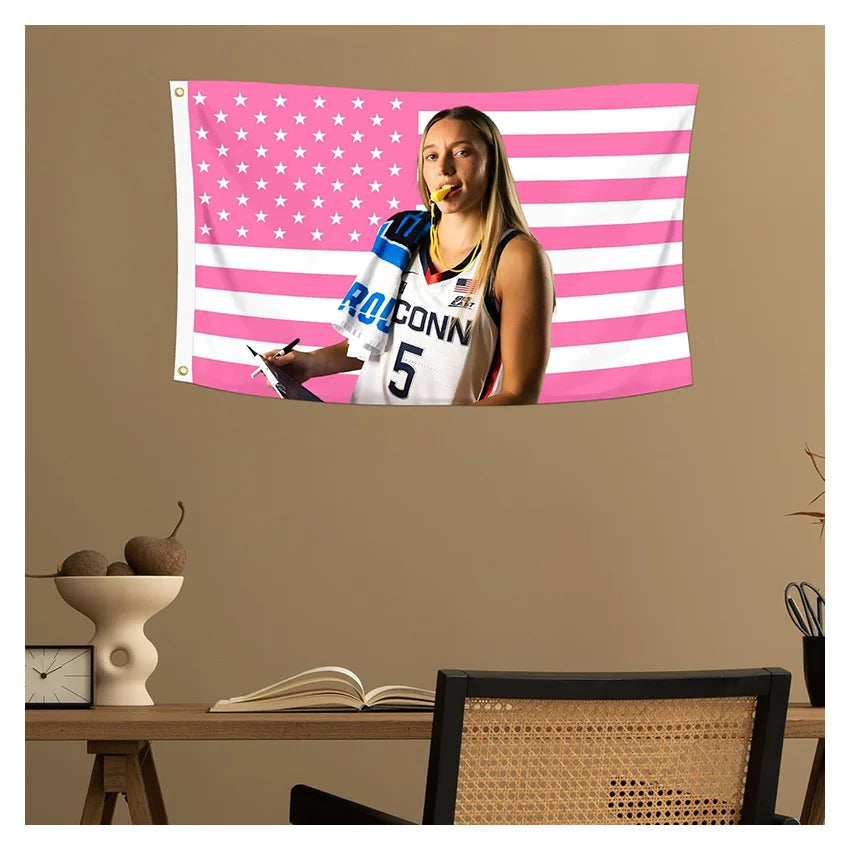 A female athlete in a sports jersey is featured on a pink and white American flag tapestry wall hanging.