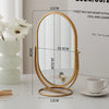 A gold-framed oval vanity mirror with measurements and a white cup is displayed on a light surface.