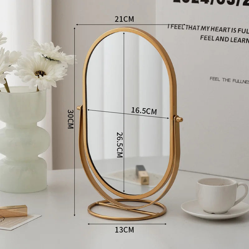 A gold-framed oval vanity mirror with measurements and a white cup is displayed on a light surface.