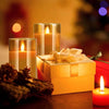 A set of LED flameless candles with flickering flame effects placed next to a gold gift box and pine cones.