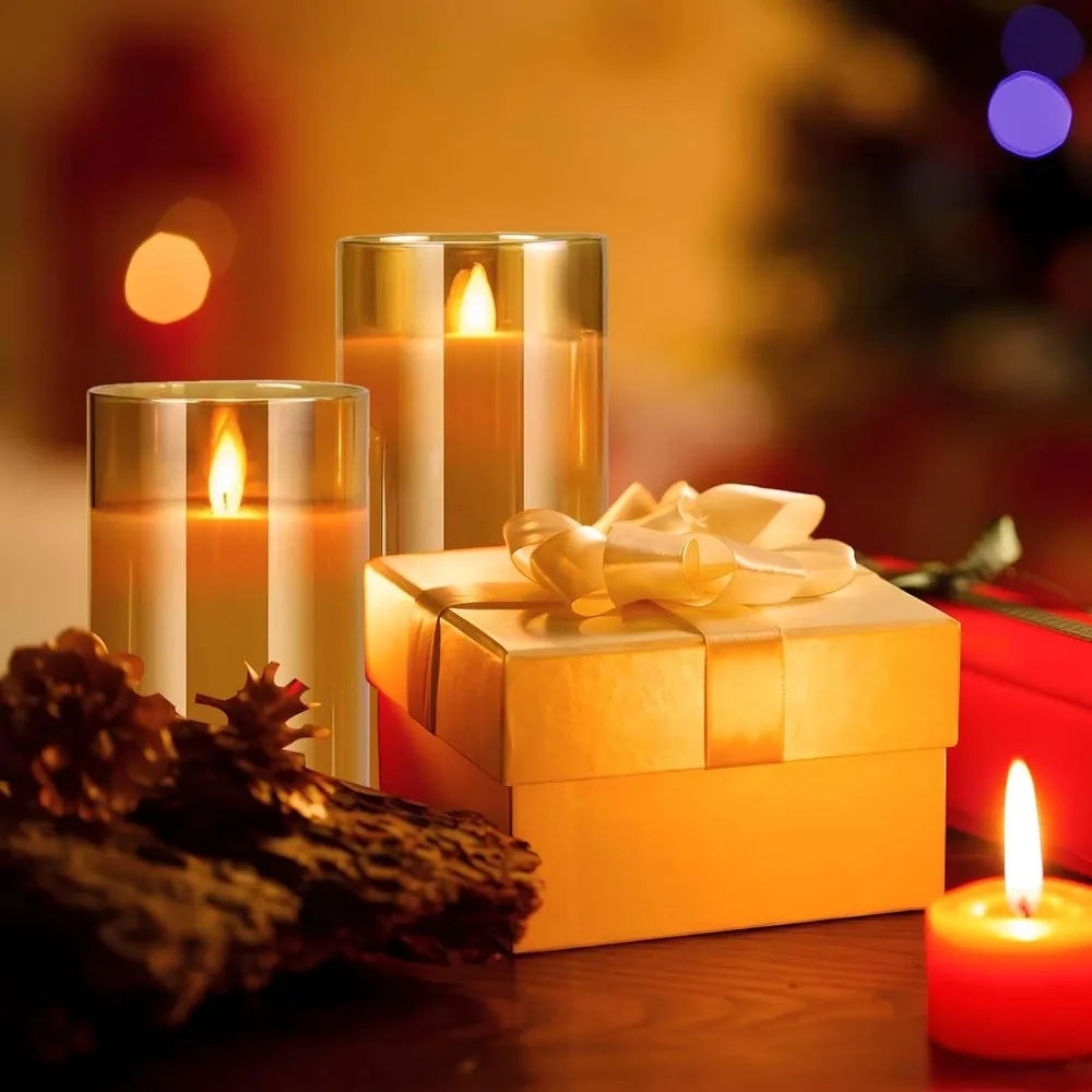 A set of LED flameless candles with flickering flame effects placed next to a gold gift box and pine cones.