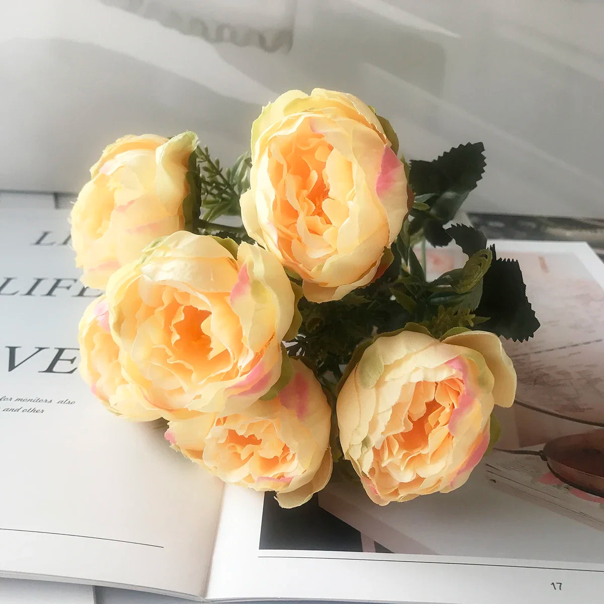 A bouquet of silk rose and peony artificial flowers in shades of yellow and peach displayed on a white page.